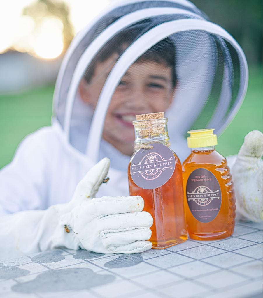 A young boy wearing white gloves and holding two bottles of honey.